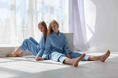 年轻的双胞胎女孩相同的蓝色的西装坐着白色圆形幻画地板上工作室模式光影子