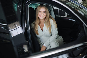 attactive年轻的业务女人坐着车<strong>车展</strong>厅女人选择车美丽的金发碧眼的头发女西装