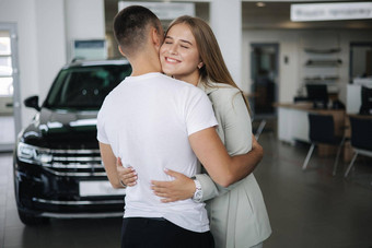快乐女人拥抱丈夫后购买车车展厅男人。女人买车