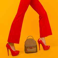女人时尚美丽的小背包手提包红色的高高跟鞋鞋子黄色的背景
