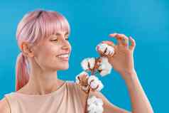 肖像快乐年轻的女人粉红色的头发微笑触碰用钉子钉上毛茸茸的棉花花摆姿势孤立的蓝色的工作室背景