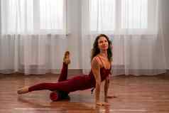 年轻的女人健身教练红色的运动服装紧身裤前伸展运动健身房普拉提瑜伽席大窗口阳光明媚的一天女健身瑜伽例程概念
