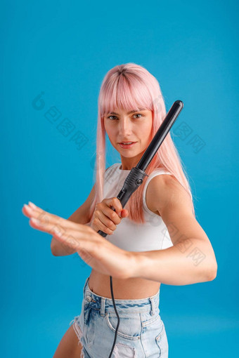 好玩的年轻的女人粉红色的头发相机使<strong>武术</strong>艺术构成持有卷曲铁摆姿势孤立的蓝色的工作室<strong>背景</strong>