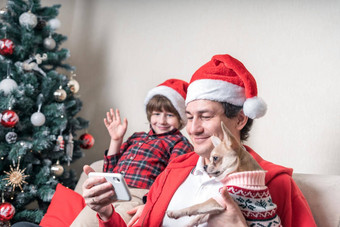 孩子父亲小狗狗圣诞老人帽子视频调用圣诞节一天坐着沙发上生活房间圣诞节树首页