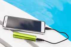 智能手机连接绿色可移植的电池充电器Usb电缆蓝色的水背景紧急充电电话懒人游泳池休息