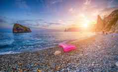 粉红色的充气床垫鹅卵石海滩日落岩石海边视图单充气床垫夏天假期背景复制空间旅行放松孤独概念