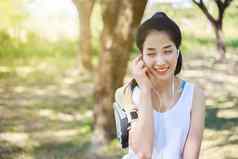 年轻的女人听音乐耳机聪明的电话应用程序公园