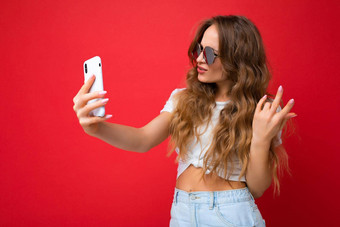 特写镜头快乐令人惊异的美丽的年轻的女人持有移动电话采取自拍照片智能手机相机穿日常时尚的装孤立的色彩斑斓的墙背景设备屏幕