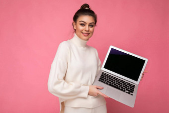 <strong>照片</strong>美丽的微笑褐色年轻的女人<strong>聚集</strong>黑暗头发穿白色毛衣持有电脑移动PC相机孤立的粉红色的墙背景