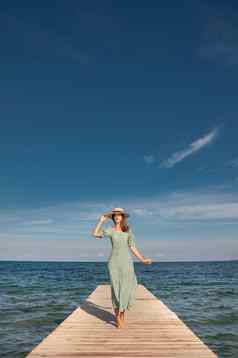 有吸引力的年轻的高加索人女人绿色衣服稻草他走木码头背景蓝色的海蓝色的天空阳光明媚的一天