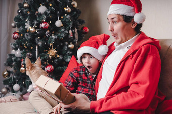 惊讶家庭圣诞老人他父亲孩子儿子开放圣诞节礼物首页坐着沙发上生活房间孩子男孩爸爸冬天圣诞节假期