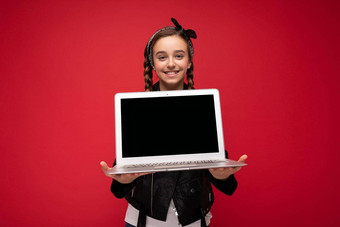 <strong>照片</strong>美丽的快乐微笑女孩褐色辫子持有电脑移动PC穿黑色的夹克大手帕孤立的红色的<strong>墙背景</strong>相机