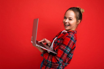 一边配置<strong>文件</strong>照片漂亮的笑年轻的女人持有上网本相机打字<strong>键盘</strong>穿红色的衬衫孤立的红色的墙背景