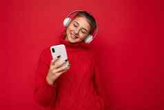 照片拍摄美丽的快乐的微笑年轻的女人穿时尚的休闲装孤立的色彩斑斓的背景墙穿白色蓝牙无线耳机听音乐移动电话gadjet显示