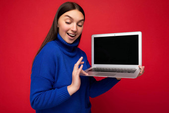 <strong>照片</strong>拍摄美丽的年轻的褐色女人持有电脑移动PC蓝色的毛衣孤立的红色的<strong>墙背景</strong>