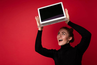 照片美丽的微笑快乐年轻的浅黑肤色的女人女人持有电脑移动PC空监控屏幕穿黑色的长袖上网本孤立的红色的背景