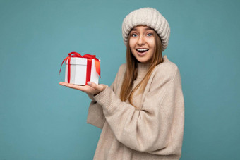 照片拍摄漂亮的积极的惊讶年轻的黑暗金发碧眼的女人孤立的色彩鲜艳的背景墙穿时尚的冬天装持有礼物盒子相机