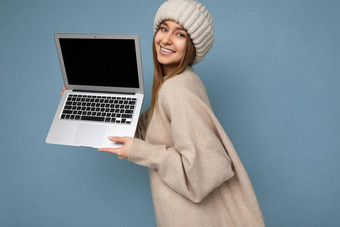 特写镜头一边配置文件照片拍摄美丽的迷人的迷人的漂亮的微笑快乐年轻的黑暗金发碧眼的女人冬天温暖的针织米色他持有电脑移动PC相机穿米色冬天毛衣孤立的光蓝色的墙背景