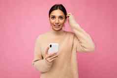 有吸引力的可爱的年轻的褐色女人穿米色温暖的毛衣站孤立的粉红色的背景冲浪互联网电话相机问题