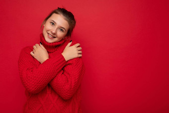 有吸引力的<strong>可爱</strong>的微笑年轻的女人穿温暖的红色的毛衣孤立的红色的<strong>背景墙</strong>保持手胸部相机