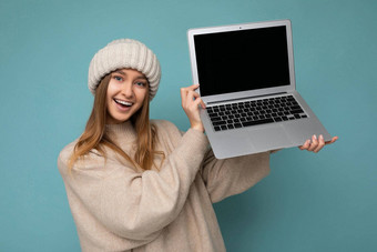 美丽的迷人的迷人的漂亮的微笑快乐年轻的黑暗金发碧眼的feemale学生女人冬天温暖的针织米色他持有电脑移动PC相机穿米色冬天毛衣孤立的光蓝色的背景工作室