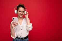 照片拍摄美丽的快乐的微笑年轻的女人穿时尚的休闲装孤立的色彩斑斓的背景墙穿白色蓝牙无线耳机听音乐移动电话相机