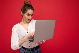 一边配置文件美丽的惊讶褐色年轻的女人持有上网本电脑开放口穿白色衬衫打字键盘孤立的红色的背景