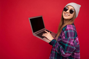一边配置文件照片美丽的微笑快乐年轻的女人持有电脑穿休闲聪明的衣服太阳镜他相机孤立的红色的背景打字键盘文本