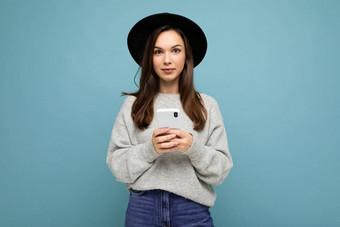年轻的浅黑肤色的女人女人穿黑色的他灰色毛衣持有智能手机相机孤立的背景