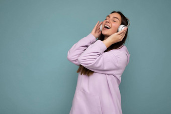 漂亮的积极的微笑年轻的浅黑肤色的女人女人穿光紫色的连帽衫孤立的蓝色的背景墙穿白色蓝牙<strong>耳机</strong>听好音乐移动有趣的