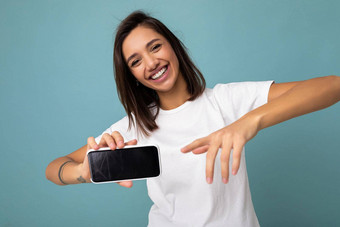 照片漂亮的积极的年轻的浅黑肤色的女人女人好穿白色t恤站孤立的蓝色的背景复制空间持有智能手机显示电话手空屏幕屏幕断路相机