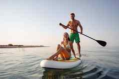 夫妇游客年轻的男人。女人有趣的paddleboarding海