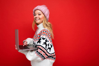 一边配置文件照片迷人的微笑快乐漂亮的年轻的女人持有移动PC孤立的红色的墙背景相机穿冬天他针织一年毛衣打字键盘