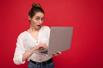 一边配置<strong>文件</strong>美丽的惊讶褐色年轻的女人持有上网本电脑相机穿白色衬衫打字<strong>键盘</strong>孤立的红色的背景