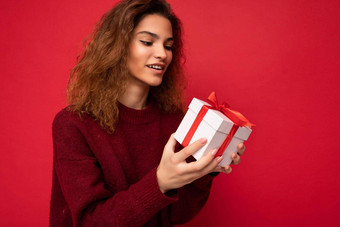 拍摄有吸引力的积极的微笑年轻的浅黑肤色的女人卷曲的女人孤立的红色的背景墙穿红色的毛衣持有礼物盒子白色盒子红色的丝带思考