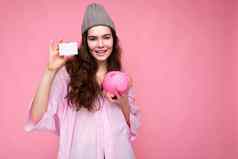 肖像美丽的积极的快乐的可爱的微笑年轻的浅黑肤色的女人女人时尚的衬衫孤立的粉红色的背景复制空间持有粉红色的猪Moneybox信贷卡模型