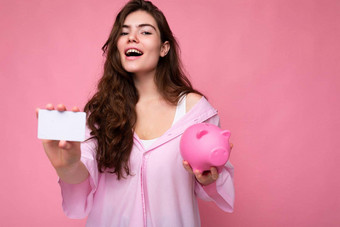 美丽的快乐快乐的年轻的浅黑肤色的女人女人穿衬衫孤立的粉红色的背景免费的空间持有粉红色的猪钱盒子信贷卡模型