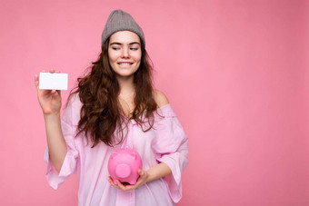 美丽的快乐快乐的微笑年轻的浅黑肤色的女人女人穿衬衫孤立的粉红色的背景免费的空间持有粉红色的猪钱盒子信贷卡模型