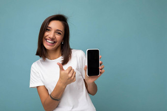 有吸引力的微笑年轻的褐色女人好穿白色t恤站孤立的蓝色的背景复制空间持有智能手机显示电话手空屏幕屏幕断路显示拇指手势