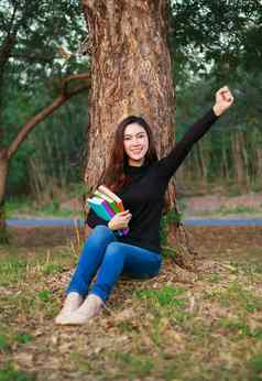 快乐的女人持有书手臂提高了公园