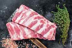 未煮过的生猪肉备用肋骨屠夫肉切肉刀黑色的背景前视图