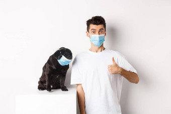 科维德动物检疫概念图像有趣的年轻的男人。小狗医疗面具老板显示拇指批准赞美白色背景