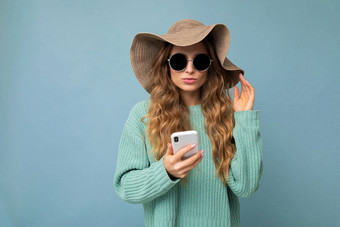美丽的年轻的金发女郎女人穿蓝色的毛衣他太阳镜站孤立的蓝色的背景冲浪互联网电话gadjet