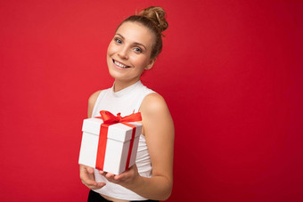 照片拍摄美丽的积极的微笑年轻的金发女郎女人孤立的红色的背景墙穿白色前持有礼物盒子相机