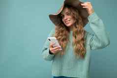 美丽的快乐微笑年轻的金发女郎女人穿蓝色的毛衣他站孤立的蓝色的背景冲浪互联网电话相机