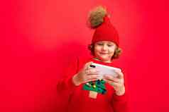 年轻的男人。智能手机手背景红色的墙针织他毛衣圣诞节树