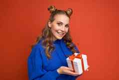 拍摄有吸引力的快乐微笑年轻的金发女郎女人孤立的红色的背景墙穿蓝色的时尚的连帽衫持有礼物盒子相机