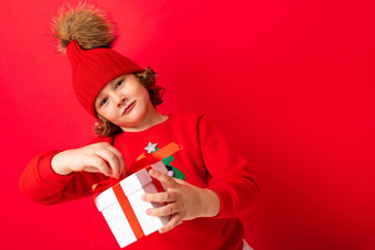 很酷的<strong>男孩</strong>卷发红色的墙背景<strong>毛衣</strong>圣诞节树持有礼物盒子手