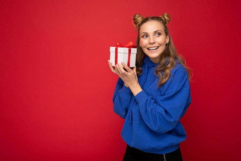 拍摄有吸引力的快乐微笑年轻的金发女郎女人孤立的红色的背景墙穿蓝色的时尚的连帽衫持有礼物盒子一边