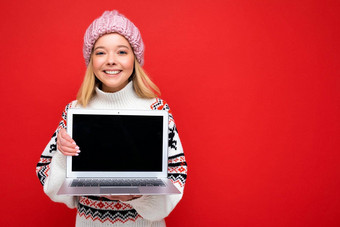<strong>照片</strong>拍摄美丽的微笑金发女郎年轻的女人持有电脑移动PC空监控屏幕模拟复制空间穿针织冬天他毛衣相机孤立的红色的<strong>墙背景</strong>